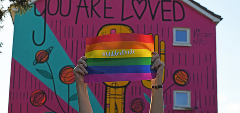 Hands holding up a rainbow #WilderPride flag
