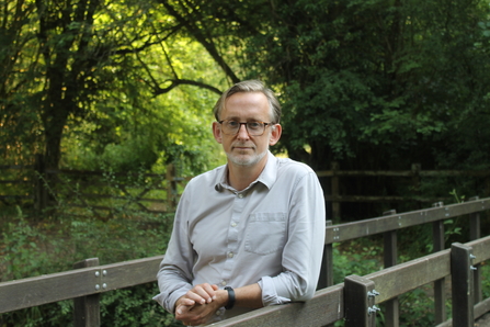 Andrew standing on a path at lower woods, with trees behind him