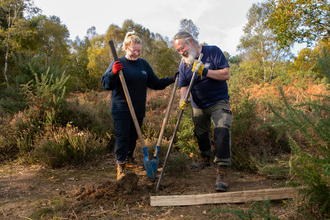 2 volunteers digging to install  post for a fence 