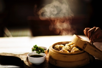 A bamboo bowl of chinese dumplings with steam rising