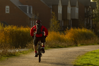 Man cycling down path by a river with houses in background