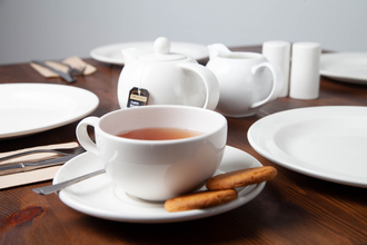 a cup of tea with two biscuits in front of a teapot and milk jug