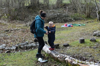 Adult helping a child walk along a log in a nature reserve