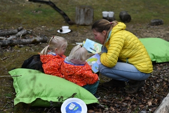 Adult reading to two children in a nature reserve