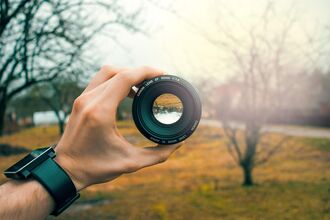A camera lens being held by a hand, framing a nature scene