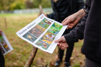 Childrens hands holding a garden minibeast spotter sheet with 10 photos of insects