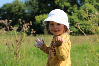 Girl_with_bug_pot in tall grass wearing white hat looking into camera
