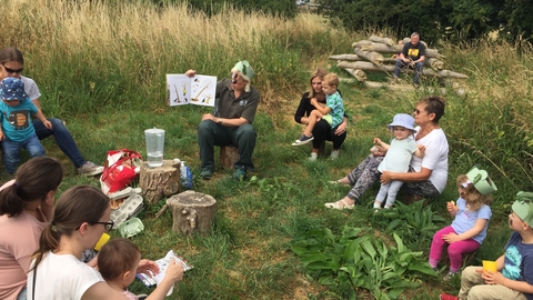 Group of children enjoying nature tots in a field GWT staff holds up example of activity