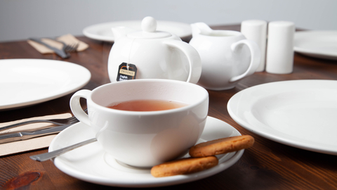 a cup of tea with two biscuits in front of a teapot and milk jug