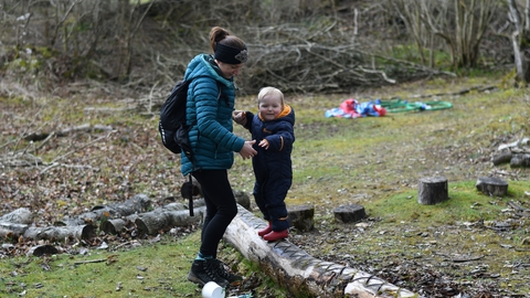 Adult helping a child walk along a log in a nature reserve