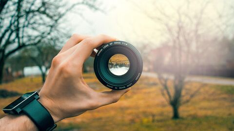 A camera lens being held by a hand, framing a nature scene