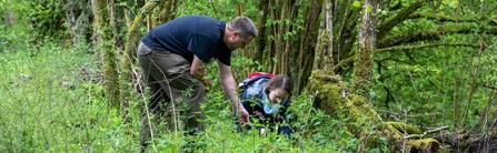 Two people in grassy woodland bent to survey plants