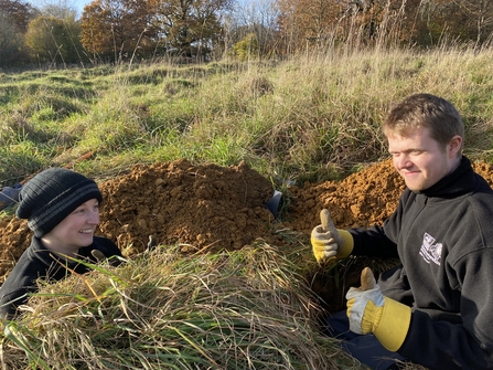 Holly and Jamie smiling at each other in large holes dug in Shortwood Pasture, Crickley Hill  
