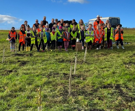 A group of children and adults behind the trees they have planted