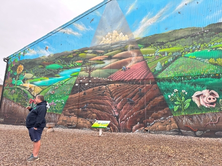 Ben in front of his mural showing what the farm was like when they first took it and what they're working towards