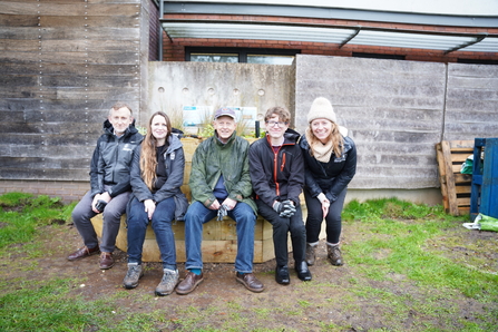 Three men and two women sit on a curved bench that surrounds a rain garden