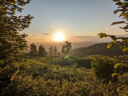 Sunset over a hilly landscape with trees and greenery