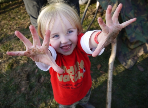 A girl with a red t shirt on holding out muddy hands