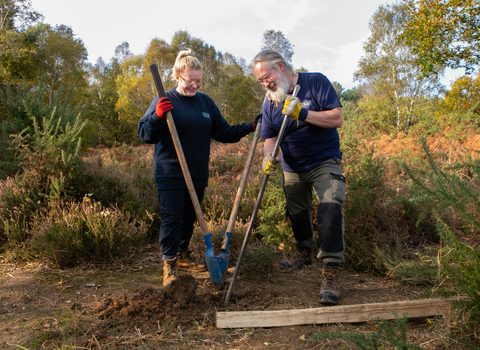 2 volunteers digging to install  post for a fence 