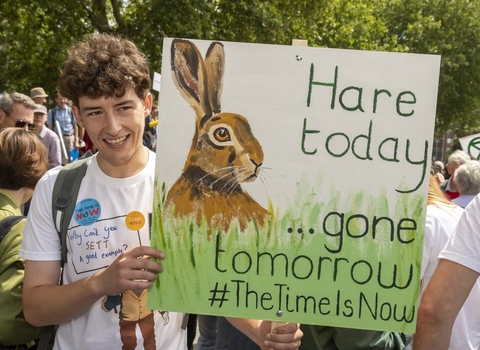 Young person holding up sign during protest that reads'Hare today...gone tomorrow #Timeisnow
