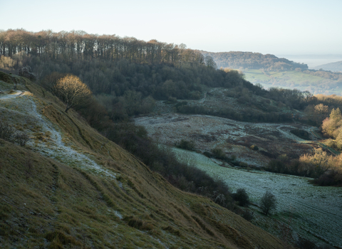 A view across Barrow Wake nature reserve with frost on the ground and the sunlight coming up over the escarpment